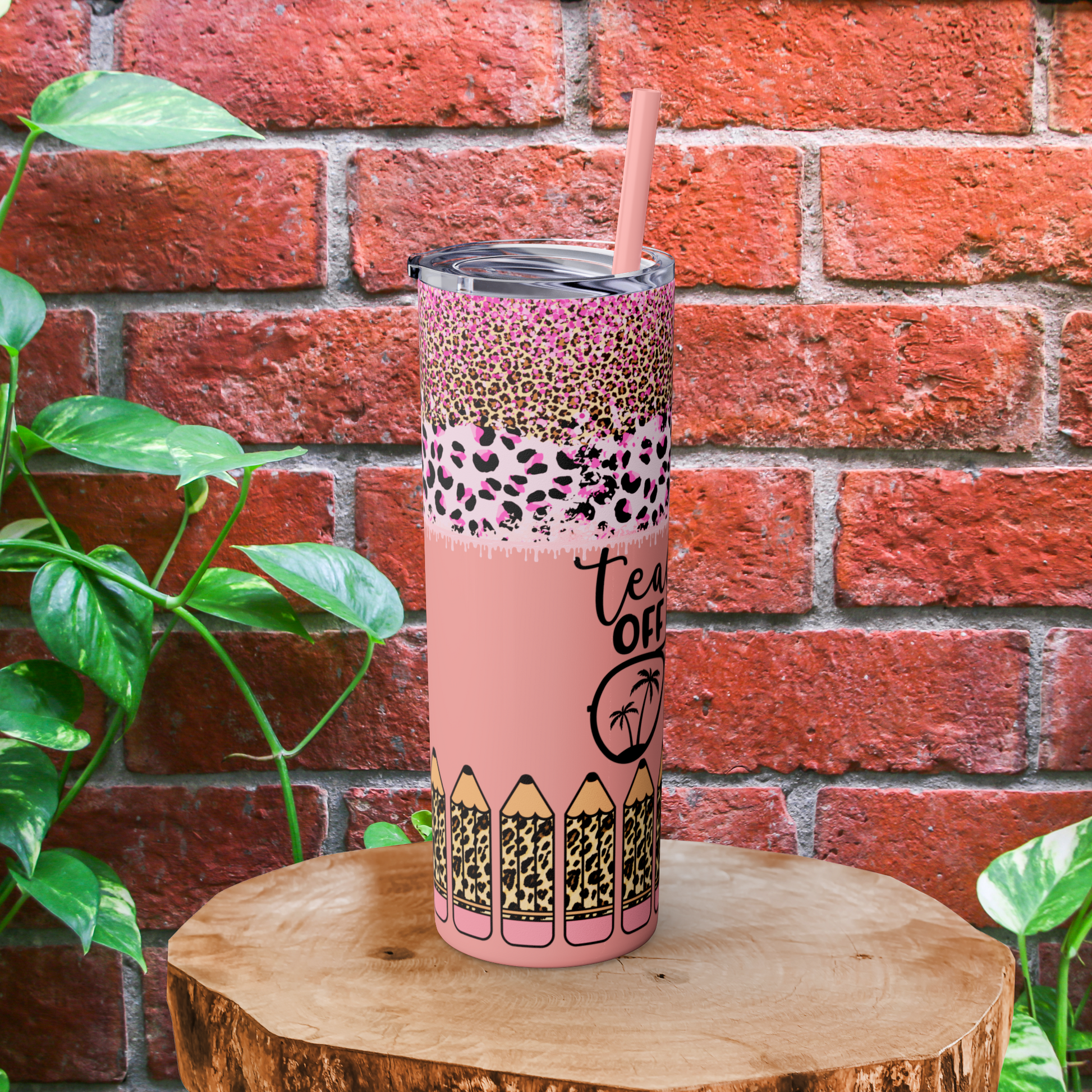 Pink tumbler with leopard print design on a wooden block against a brick wall.